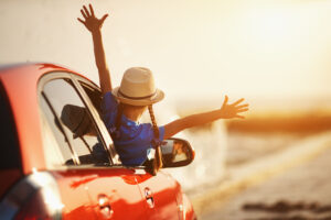 Kobieta w kapeluszu z rozłożonymi rękami wyglądająca z auta w podróży