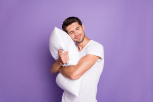 Młody mężczyzna przytulający białą poduszkę