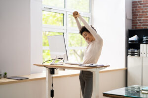 Młoda kobieta przeciąga się podczas pracy na stojąco przy biurku