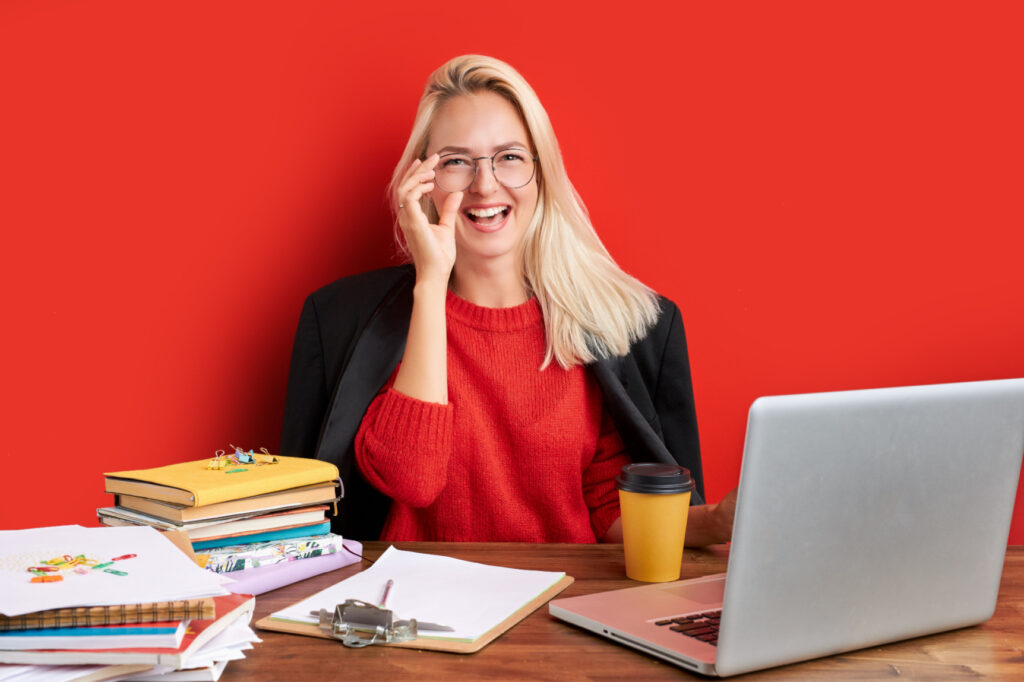 Bizneswoman siedząca przy biurku w czerwonym swetrze na czerwonym tle