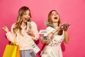 Dwie młode kobiety z torbą zakupową rozrzucają banknoty ze śmiechem