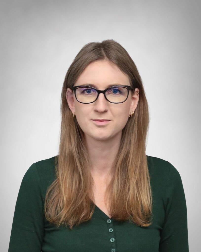 Martyna Jakimowicz w okularach z ciemnymi oprawkami i z rozpuszczonymi włosami na szarym tle.